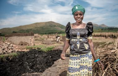 A woman, Cinama, stands and smiles proudly. Behind her is a foundation of bricks