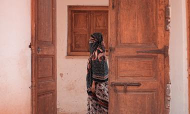 A woman walks alone past an empty room. 