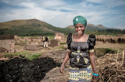 A woman, Cinama, stands and smiles proudly. Behind her is a foundation of bricks